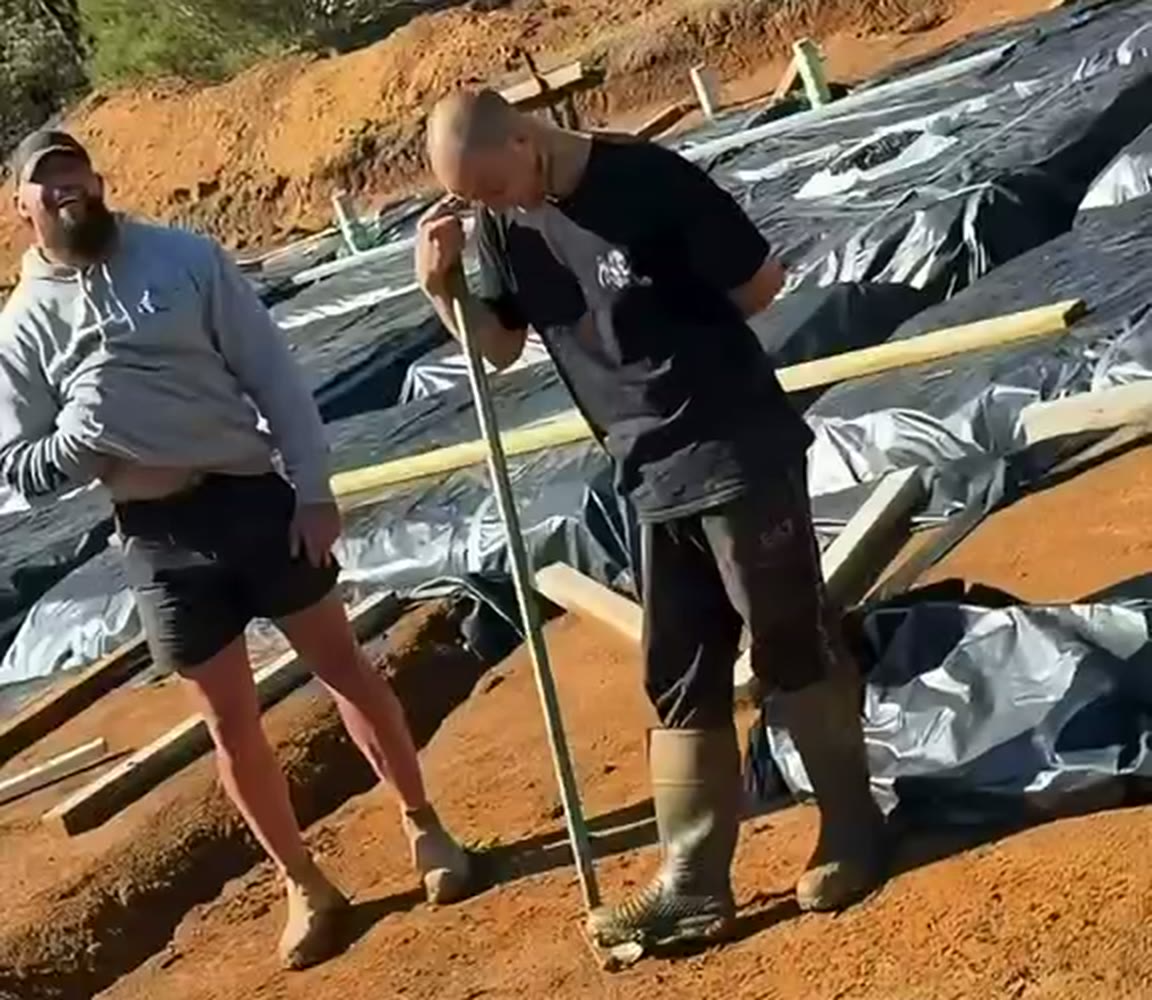 Sleeble, the former White Flash, grins while leaning on a shovel in gumboots on a Grilla site as a bearded crew member laughs beside him.